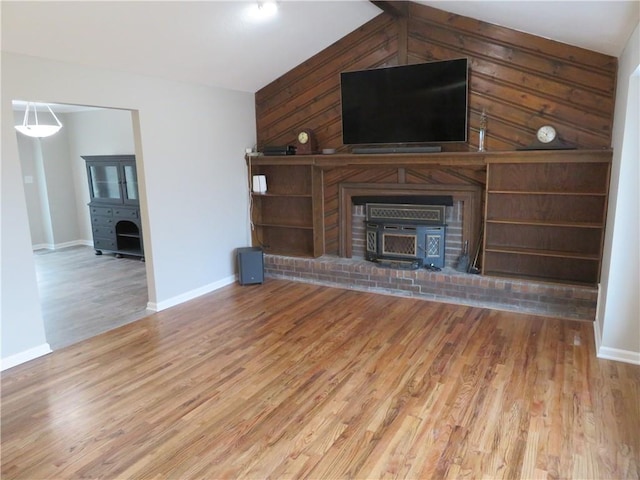 24243 Sandusky Rd, Tonganoxie, KS 66086 - unfurnished living room featuring wood finished floors, baseboards, vaulted ceiling, wooden walls, and a wood stove