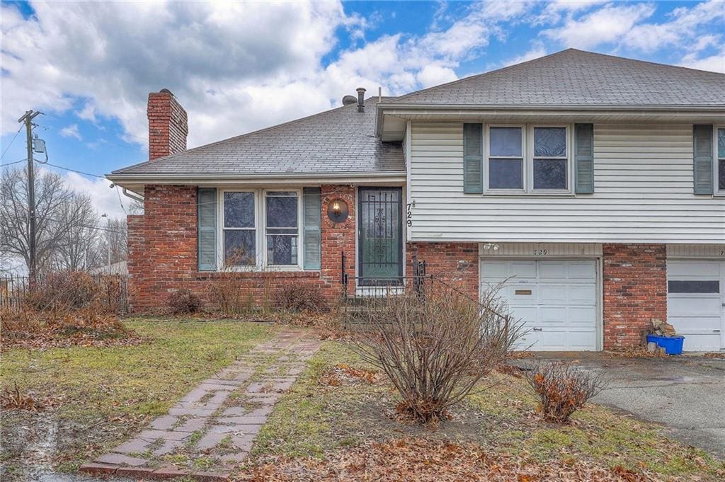 split level home featuring an attached garage, a chimney, aphalt driveway, and brick siding