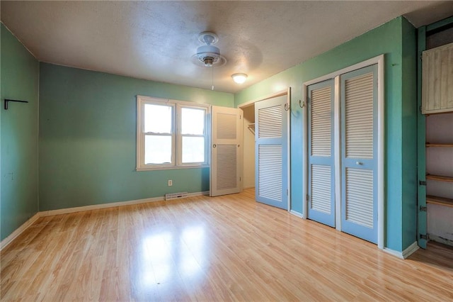 unfurnished bedroom with light wood-style flooring, visible vents, baseboards, and two closets