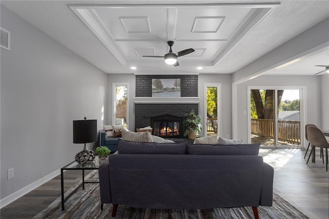 living area with baseboards, dark wood finished floors, a ceiling fan, a tray ceiling, and a fireplace