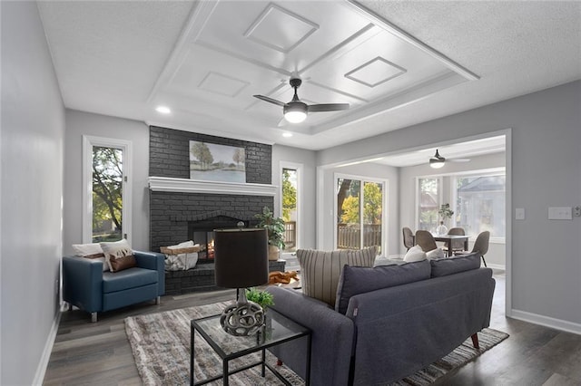 living room with a brick fireplace, a textured ceiling, baseboards, and wood finished floors