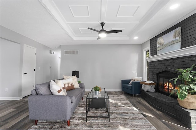 living room featuring baseboards, visible vents, wood finished floors, a tray ceiling, and a brick fireplace