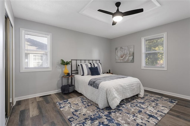 bedroom with ceiling fan, a raised ceiling, wood finished floors, and baseboards