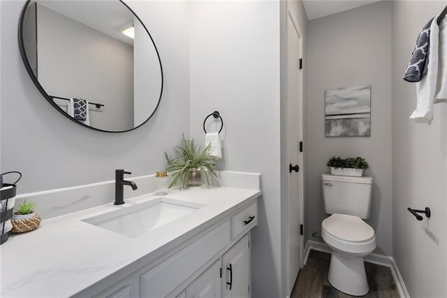 half bath featuring wood finished floors, vanity, toilet, and baseboards