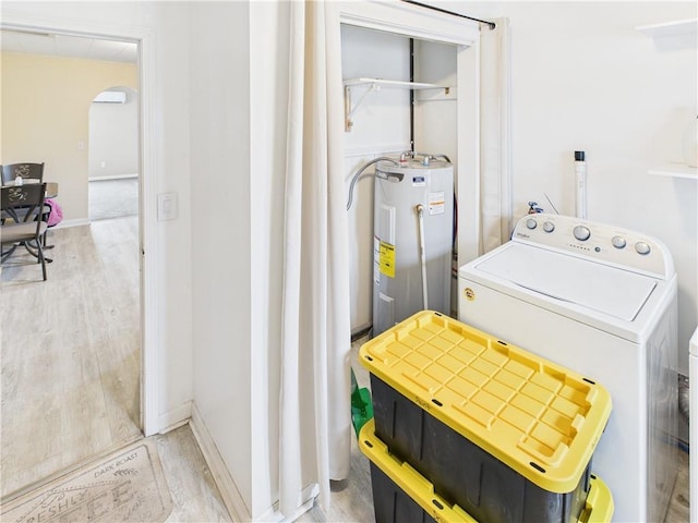 clothes washing area featuring arched walkways, washer / clothes dryer, electric water heater, laundry area, and baseboards