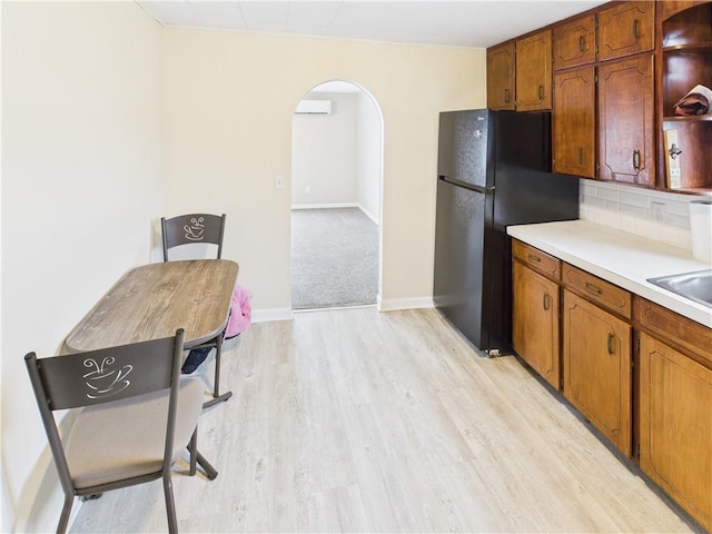 kitchen with arched walkways, brown cabinets, light countertops, light wood-style floors, and freestanding refrigerator