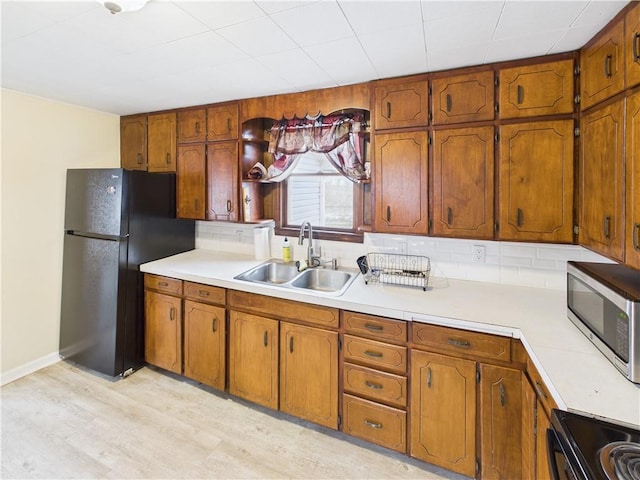 kitchen featuring light countertops, brown cabinets, a sink, and black appliances