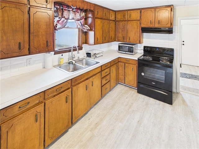 kitchen featuring stainless steel microwave, brown cabinets, black electric range, under cabinet range hood, and a sink