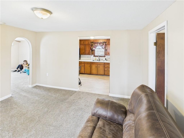 living area with arched walkways, light colored carpet, and baseboards