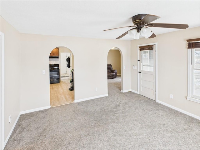 unfurnished room with light carpet, baseboards, arched walkways, and ceiling fan