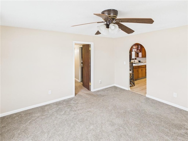 spare room with baseboards, arched walkways, light colored carpet, ceiling fan, and a sink