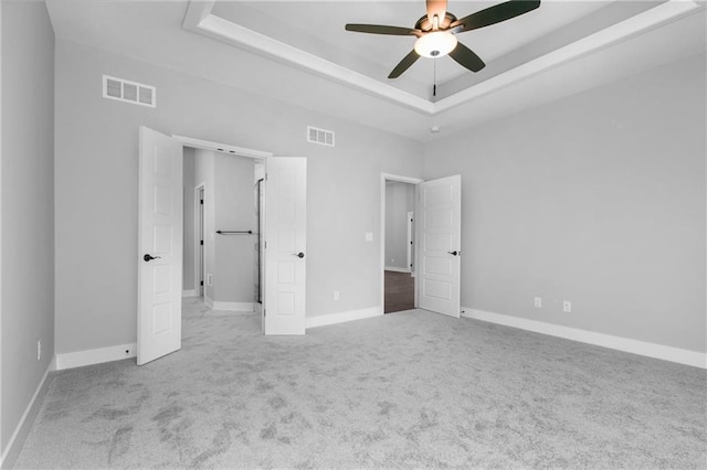 unfurnished bedroom with carpet, visible vents, a raised ceiling, and baseboards