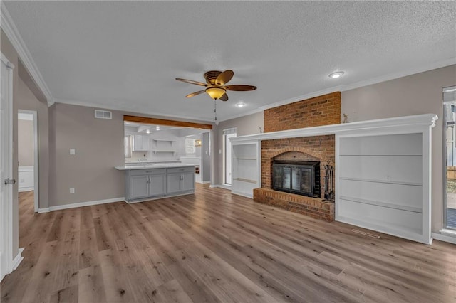 unfurnished living room featuring visible vents, a textured ceiling, a brick fireplace, and ornamental molding