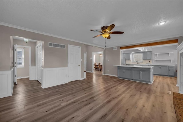 unfurnished living room featuring visible vents, a textured ceiling, a wainscoted wall, and wood finished floors