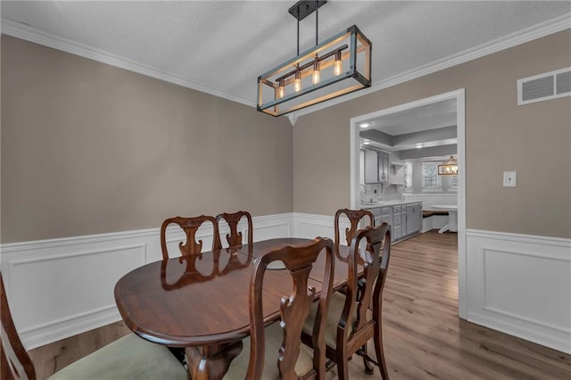 dining area featuring a wainscoted wall, ornamental molding, visible vents, and wood finished floors