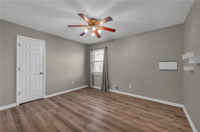 empty room with visible vents, baseboards, wood finished floors, a textured ceiling, and a ceiling fan