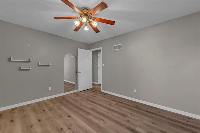 unfurnished bedroom featuring visible vents, arched walkways, baseboards, and wood finished floors