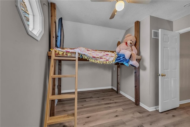 unfurnished bedroom featuring visible vents, a textured ceiling, wood finished floors, baseboards, and ceiling fan