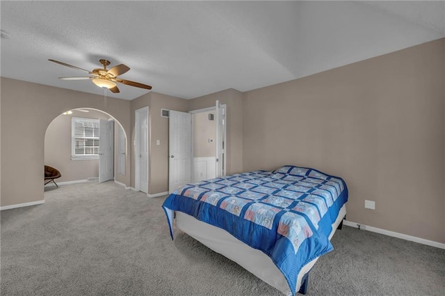 carpeted bedroom featuring ceiling fan, arched walkways, baseboards, and a textured ceiling