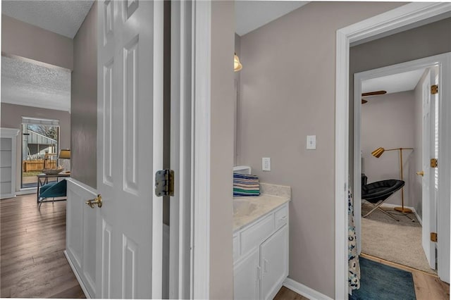 bathroom with a textured ceiling, vanity, baseboards, and wood finished floors