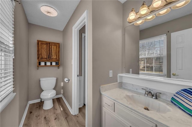 bathroom featuring baseboards, toilet, wood finished floors, and vanity