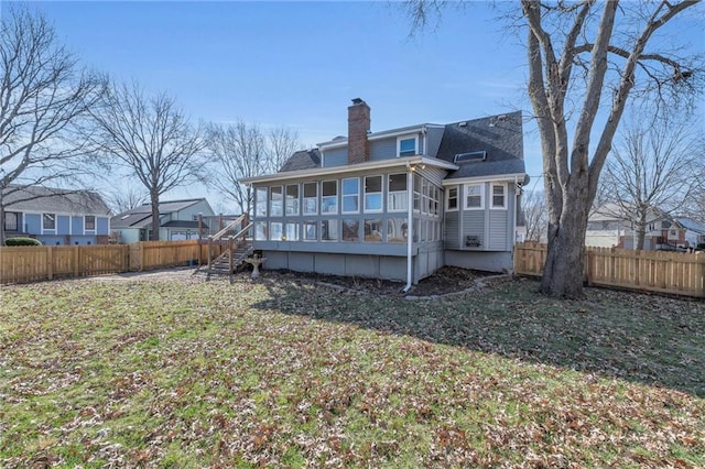 rear view of property with a lawn, a chimney, a fenced backyard, a sunroom, and stairs