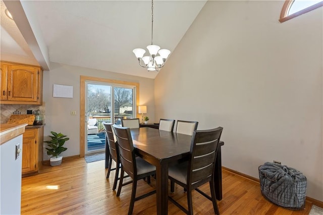 dining room featuring baseboards, light wood-style floors, an inviting chandelier, and high vaulted ceiling