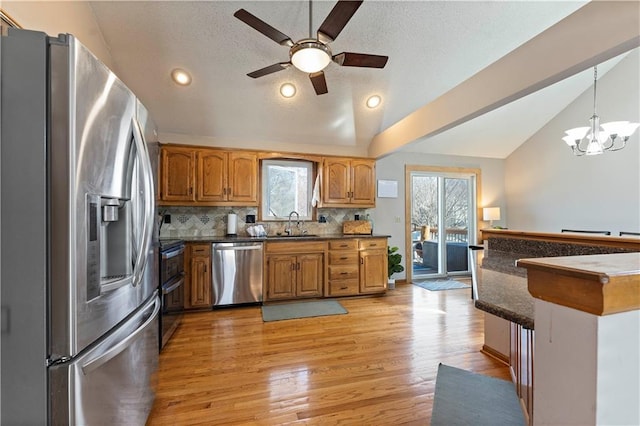 kitchen with light wood-type flooring, lofted ceiling, brown cabinets, ceiling fan with notable chandelier, and stainless steel appliances