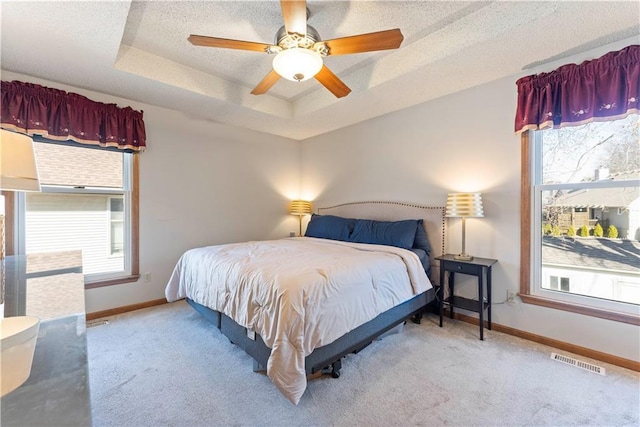 bedroom with a raised ceiling, multiple windows, and visible vents