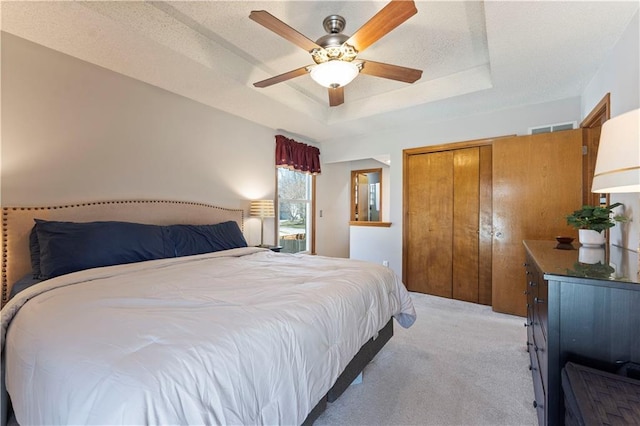 bedroom with visible vents, light colored carpet, a tray ceiling, a closet, and a ceiling fan