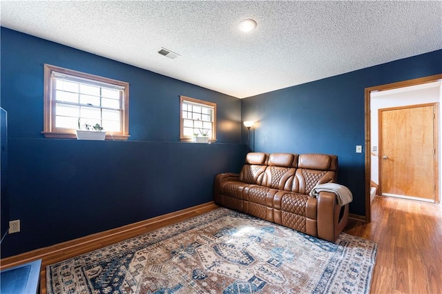 living room with visible vents, a textured ceiling, baseboards, and wood finished floors