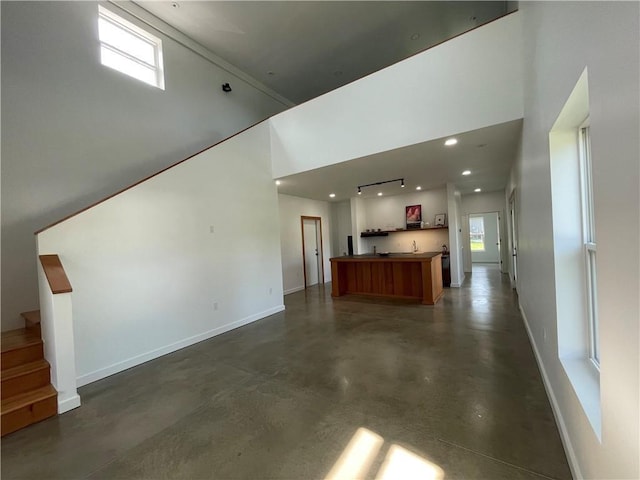 unfurnished living room featuring finished concrete floors, baseboards, stairway, and a high ceiling