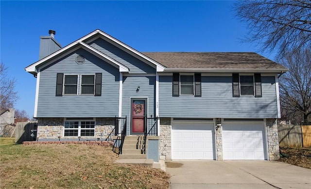 raised ranch with stone siding, an attached garage, a chimney, and fence