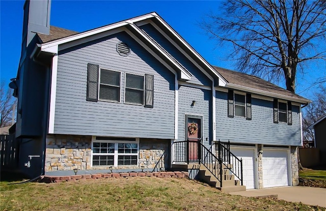 bi-level home with a chimney, stone siding, concrete driveway, and a garage