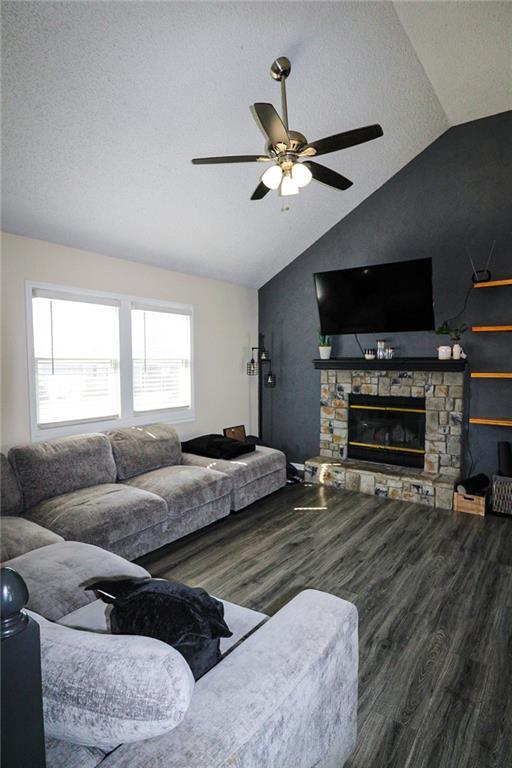 living area with lofted ceiling, a stone fireplace, wood finished floors, a textured ceiling, and a ceiling fan