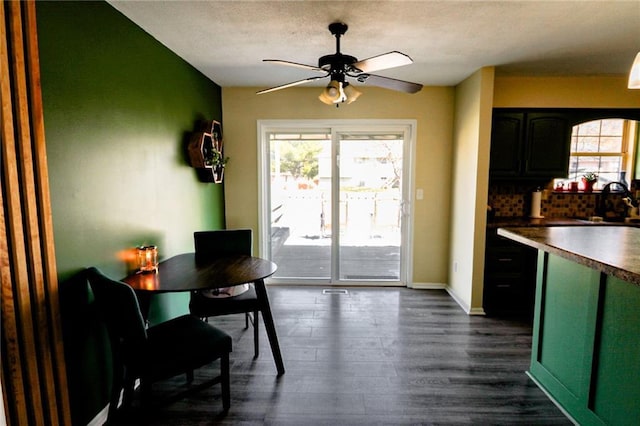 kitchen with dark countertops, backsplash, dark wood-type flooring, ceiling fan, and baseboards