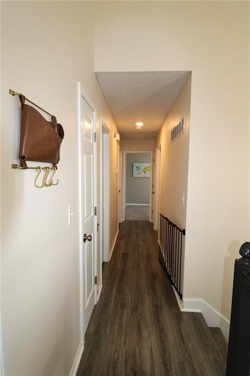 hall with dark wood-style floors, visible vents, a textured ceiling, and baseboards