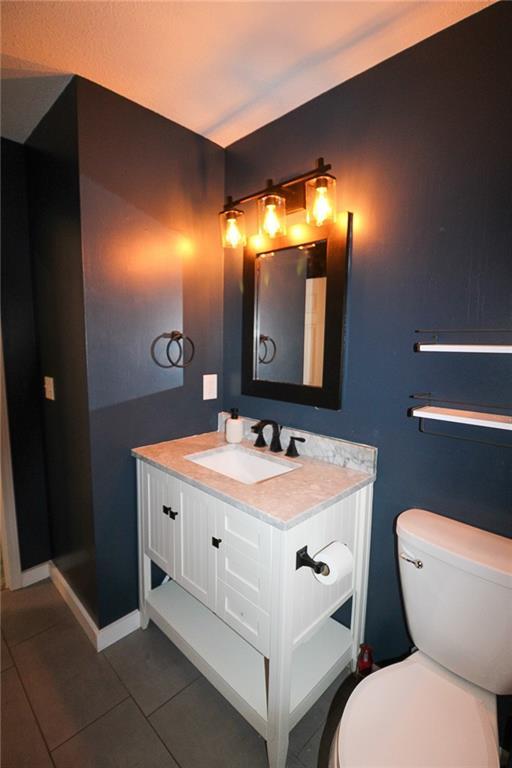 half bathroom featuring tile patterned floors, toilet, vanity, and baseboards