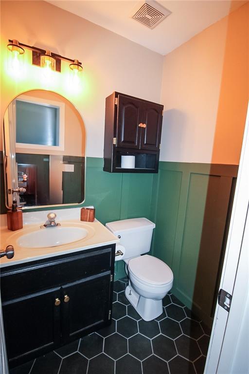 half bathroom featuring vanity, a wainscoted wall, visible vents, tile patterned floors, and toilet