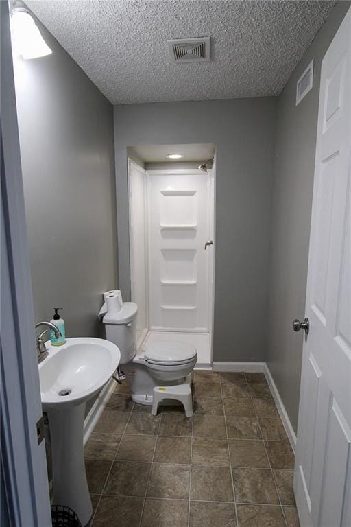 bathroom with visible vents, baseboards, toilet, a stall shower, and a textured ceiling