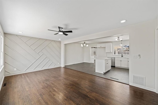 unfurnished living room featuring visible vents, dark wood-type flooring, a ceiling fan, and an accent wall