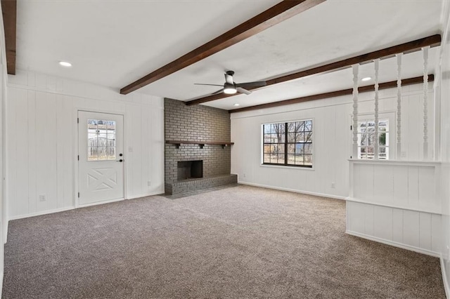 unfurnished living room featuring a ceiling fan, baseboards, beam ceiling, a fireplace, and carpet flooring