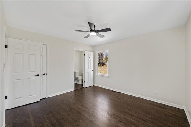 unfurnished bedroom with ceiling fan, baseboards, dark wood-type flooring, and ensuite bath