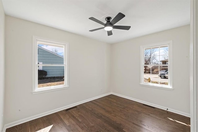 empty room featuring dark wood-style floors, visible vents, a ceiling fan, and baseboards