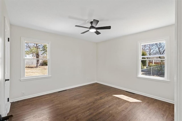 spare room featuring ceiling fan, visible vents, baseboards, and dark wood finished floors