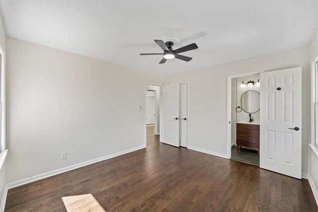 unfurnished bedroom with a ceiling fan, ensuite bathroom, baseboards, and dark wood-style flooring