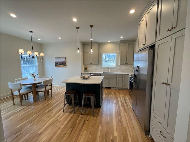 kitchen featuring a center island, light countertops, gray cabinetry, stainless steel refrigerator with ice dispenser, and a sink