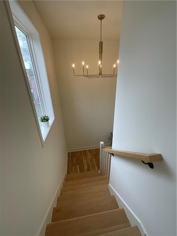 stairs featuring a notable chandelier, baseboards, and wood finished floors