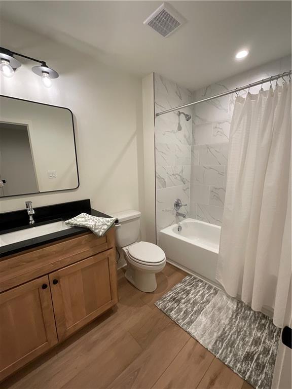 full bath with shower / bath combo, visible vents, toilet, wood finished floors, and vanity