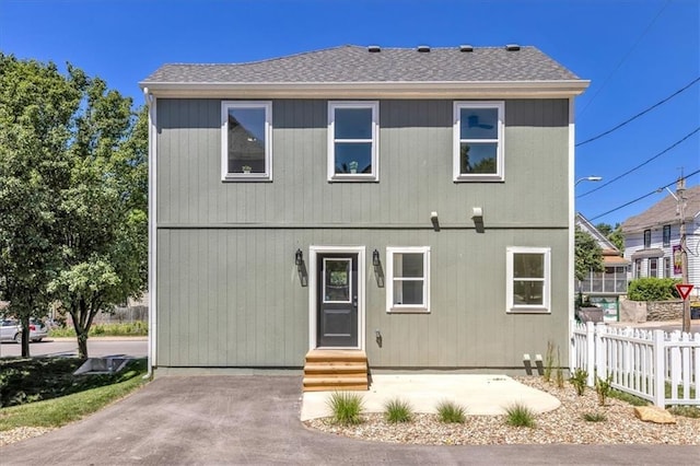 view of front facade featuring entry steps, roof with shingles, fence, and a patio